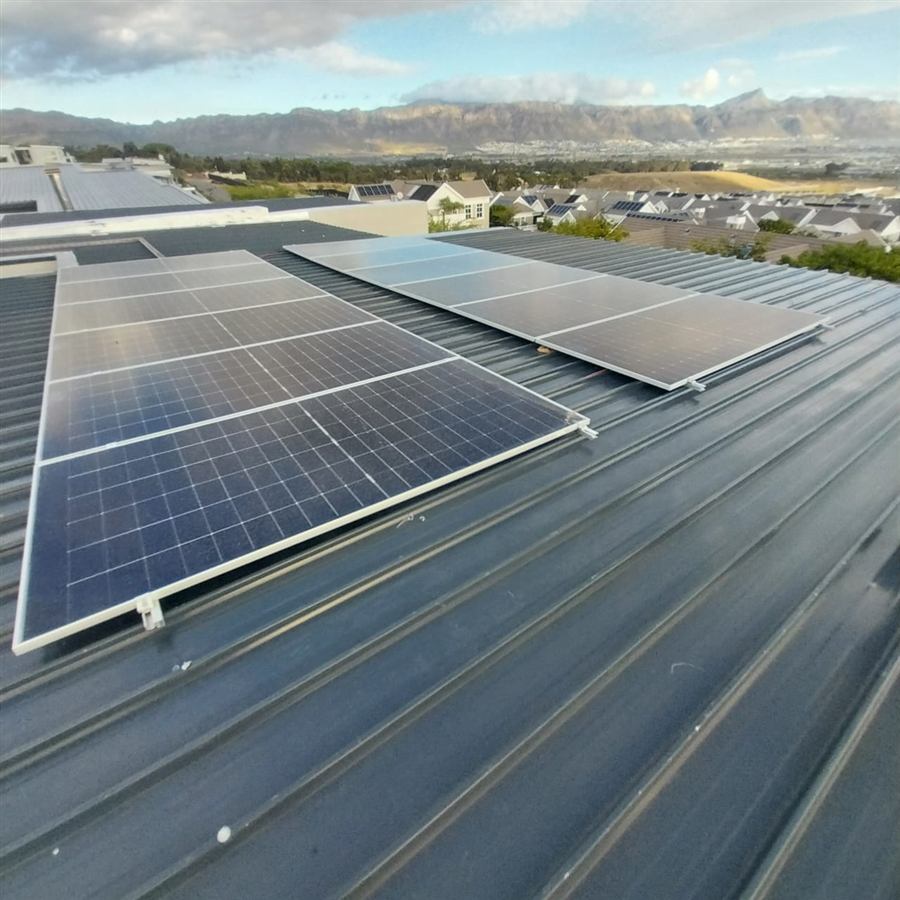 Two rows of solar panels on a metal roof with mountains in the distance
